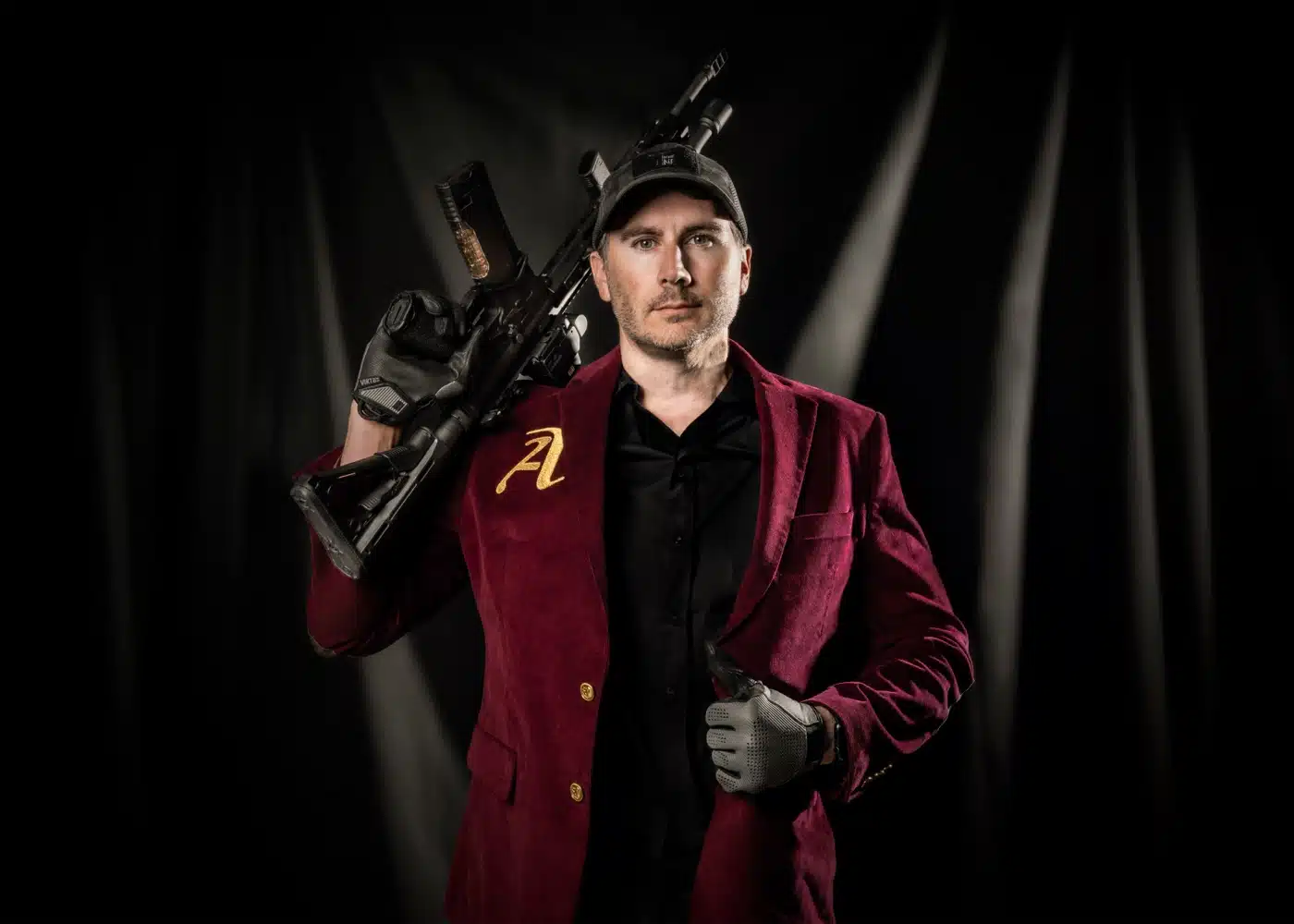 Jeremy Tremp wearing the crimson Cantius Award jacket with its gold embroidered A, a rifle resting on his shoulder.