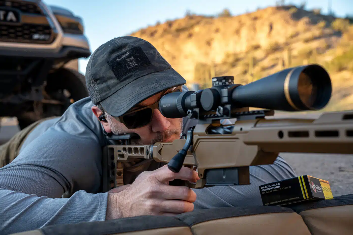 Jeremy Tremp shooting a scoped bolt-action rifle from a prone position in the desert.