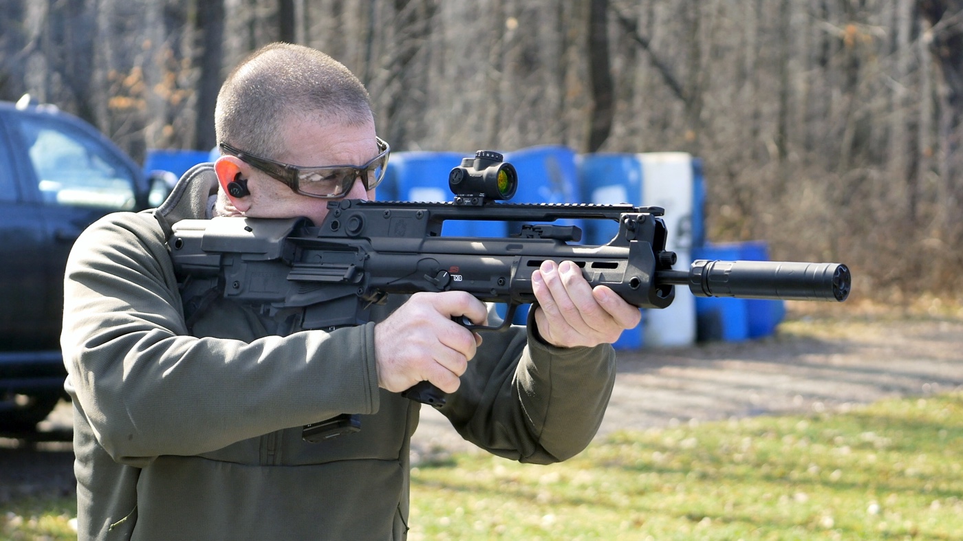 Paul Carlson shoulders a suppressed Springfield Armory Hellion bullpup rifle on an outdoor range.