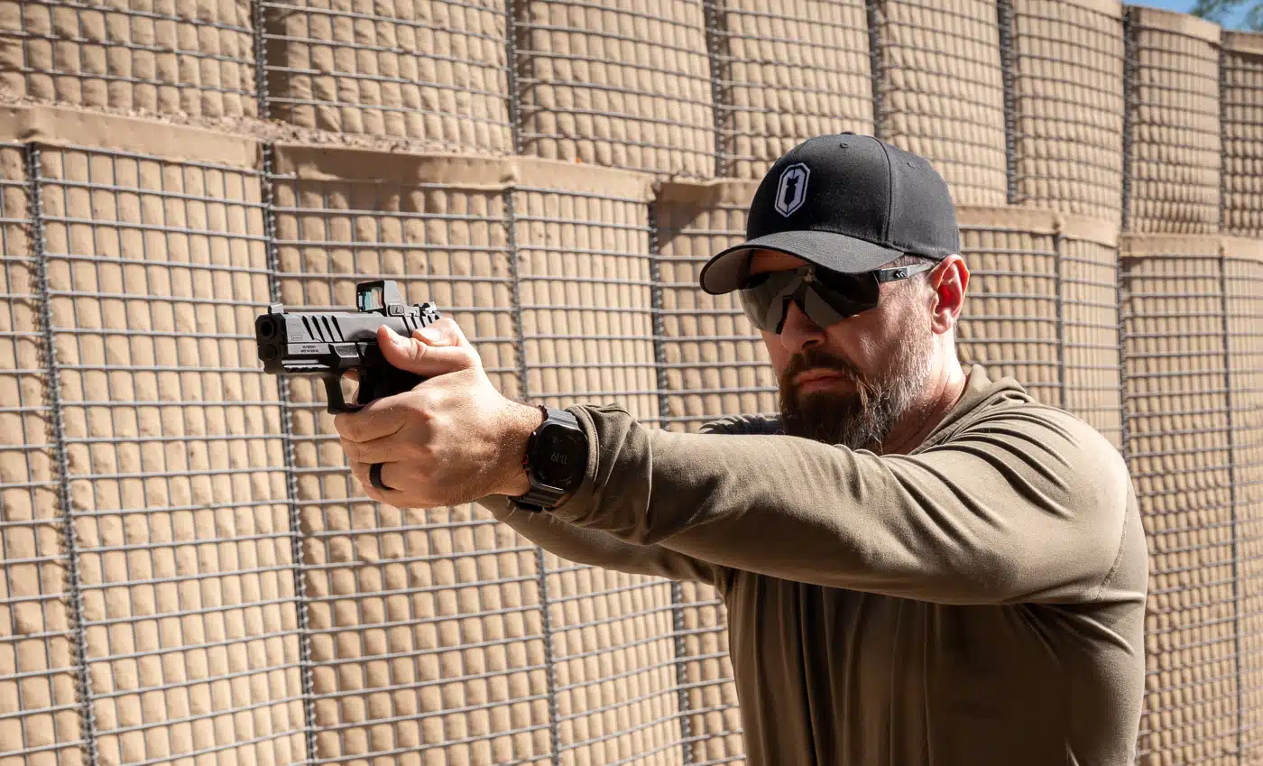 Scott Conditt firing an optic-equipped pistol on an outdoor range in front of a barrier wall.